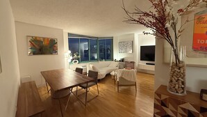 A living room with a dining table, a white sofa, and a TV. - Newport Apartment (Jersey City)
