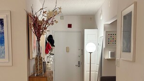 A hallway with wooden flooring, a wooden cabinet, a vase with branches, and a floor lamp. - Newport Apartment (Jersey City)