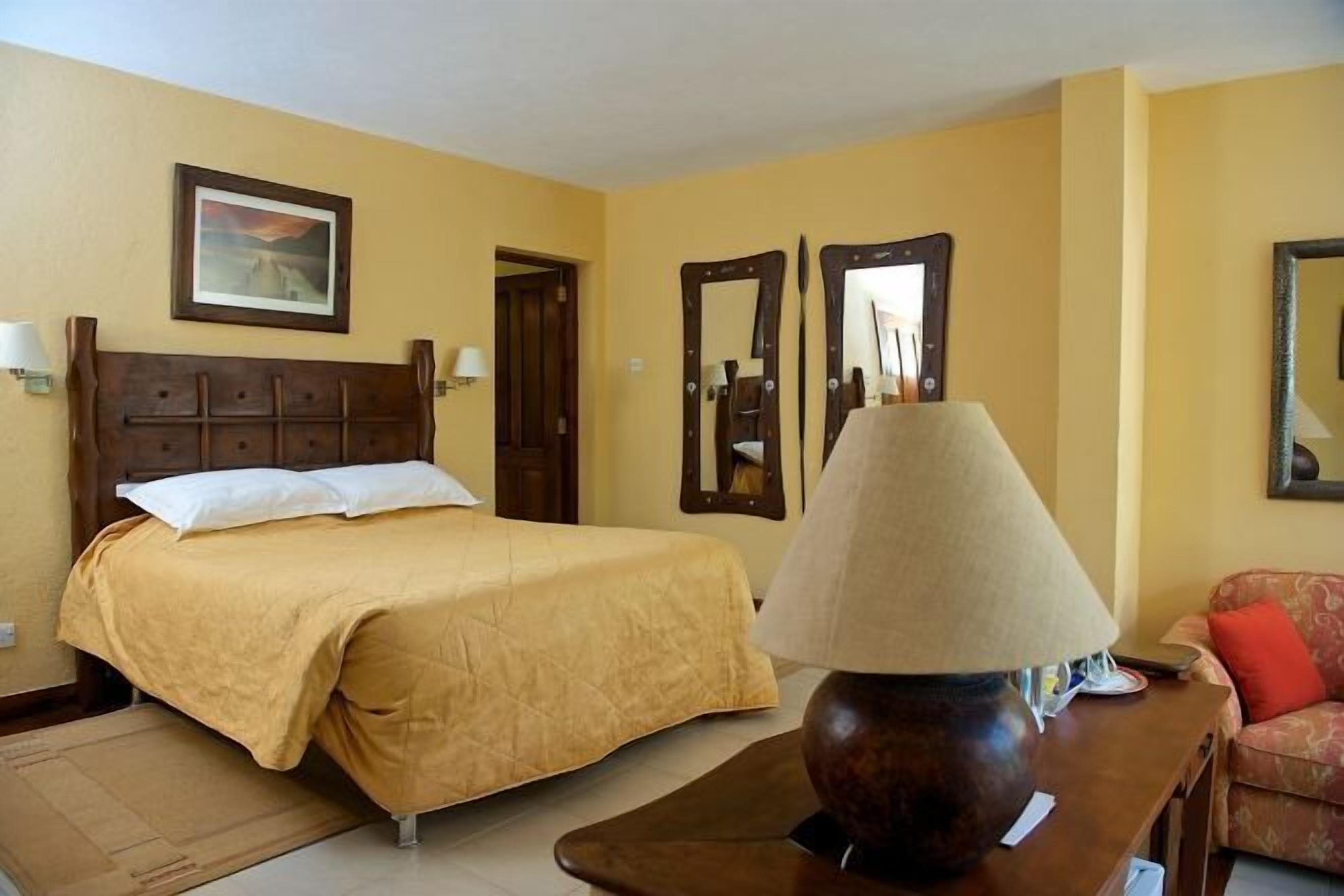 Una habitación de hotel con una cama, una mesita de noche de madera, una lámpara, un sofá y dos espejos en la pared.