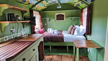 Una habitación acogedora con un mural de un paisaje, una cama, una mesita y un ventanal con cortinas.