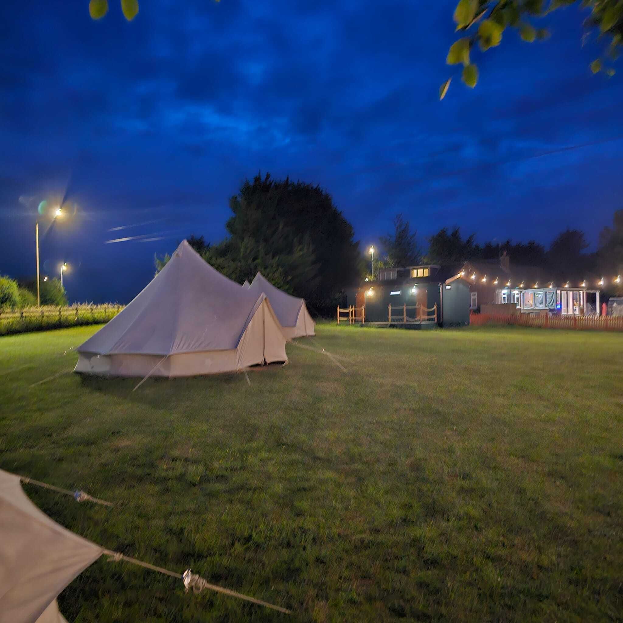 Camp de gespa amb tendes i un edifici amb llums.