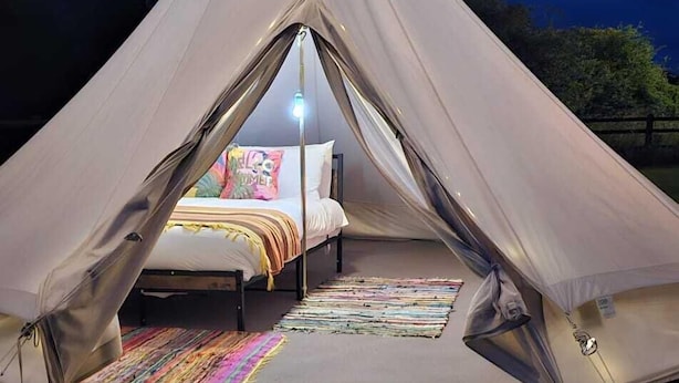 Une tente avec un lit à l’intérieur, un tapis coloré et un panneau posé au sol.