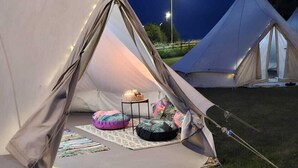 Une tente installée sur une pelouse, avec une petite table et des coussins à l’intérieur.