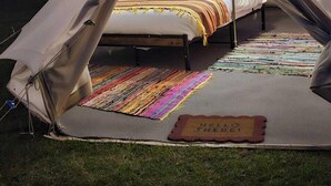 Une tente avec un lit à l’intérieur, un tapis coloré et un paillasson sur lequel est écrit « Bonjour ! ».