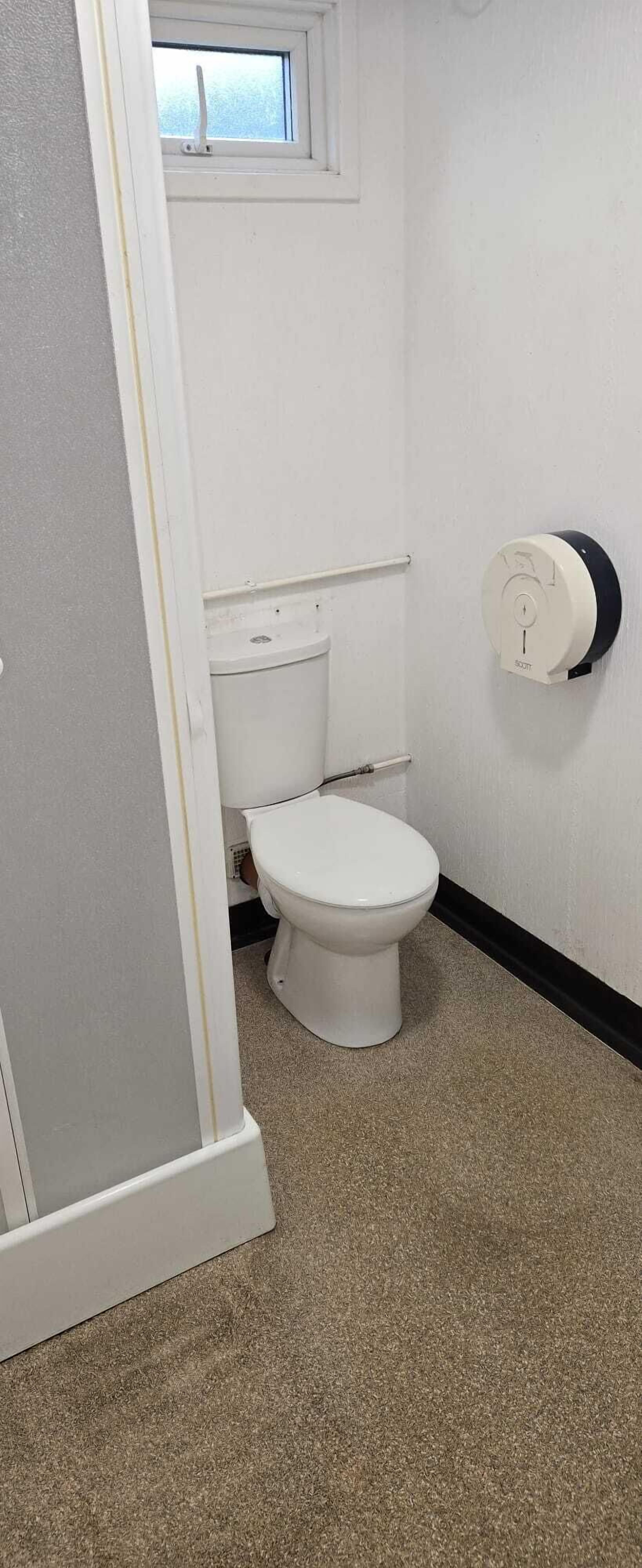 A small, white bathroom with a toilet, a towel rack, and a window.