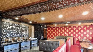 Interior de restaurante com teto em padrão hexagonal, área de bar com bancada de mármore e assentos estofados em vermelho.