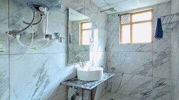 A bathroom with a white toilet, a sink with a mirror, a shower area, and a window with a towel hanging on the wall.