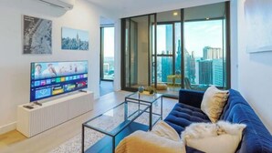 Een moderne woonkamer met een grote flatscreen-tv, een bank, een salontafel en grote ramen met uitzicht op de stad.