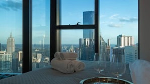 Hotelkamer in een hoog gebouw met een panoramisch stadszicht, een keurig gevouwen handdoek en een dienblad met wijnglazen.