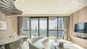 Ein modernes Wohnzimmer mit einer gebogenen Couch, einem Essbereich mit einem Marmortisch und einem großen Fernseher an der Wand.
