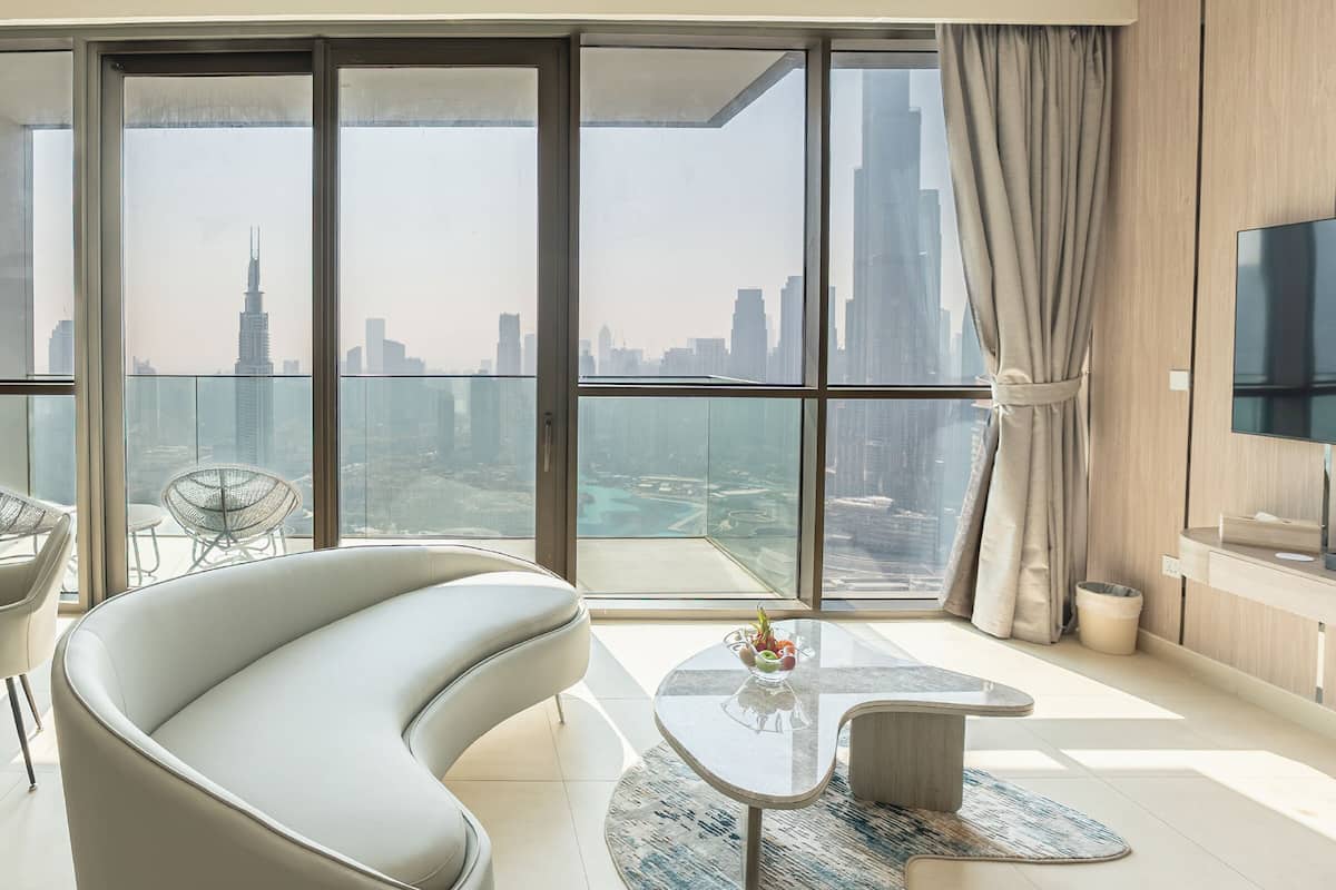 A modern living room with a curved sofa, a glass coffee table, and a view of a city skyline through large windows.