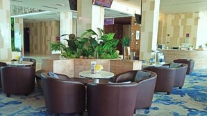 Un hall d’entrée avec un espace détente comprenant des canapés en cuir marron et une table ronde, le tout agrémenté de plantes en pot.
