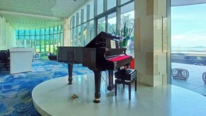 Un magnifique piano à queue dans un hall spacieux, doté de grandes fenêtres et d’un tapis à motifs bleus.