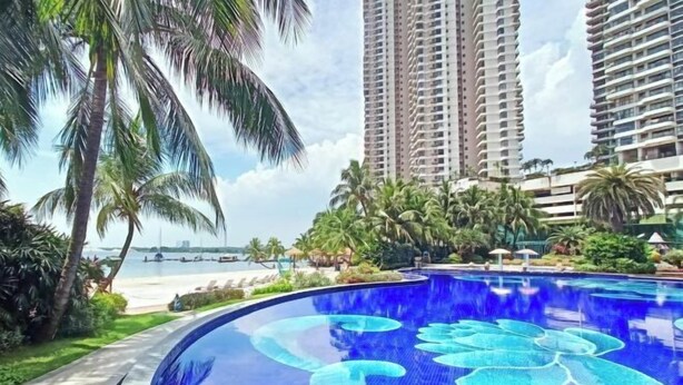 Une piscine au décor bleu, entourée de palmiers et de grands immeubles.