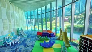 Une salle de jeux dotée d’installations colorées, d’un toboggan et d’une grande fenêtre donnant sur un paysage verdoyant.