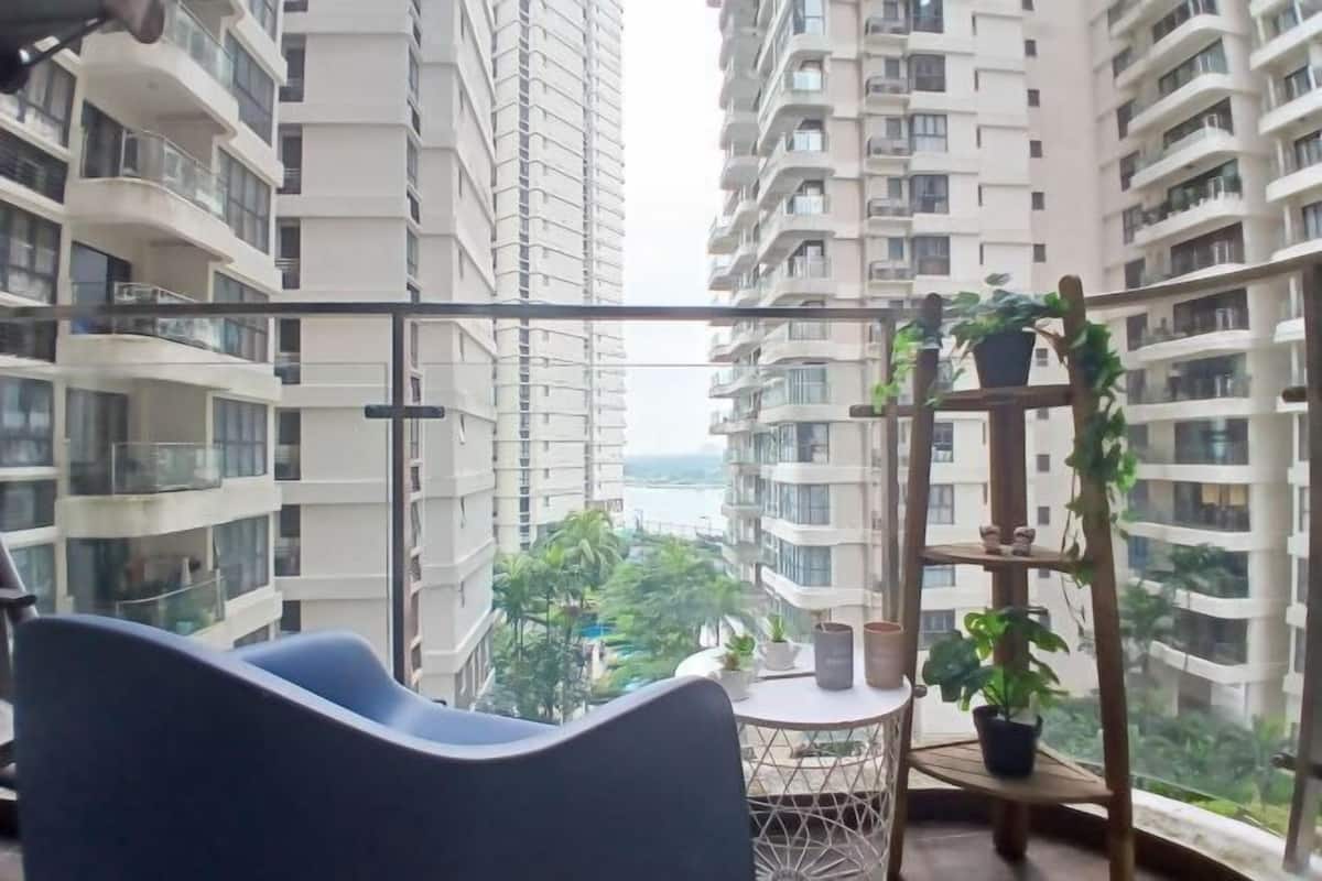 Un balcón con vistas a edificios altos, una silla azul, una pequeña mesa redonda y plantas en macetas.
