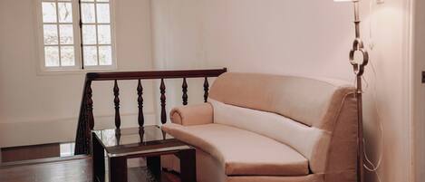 A room with a curved sofa, a glass coffee table, a wooden floor, a staircase with a wooden railing, and a floor lamp.