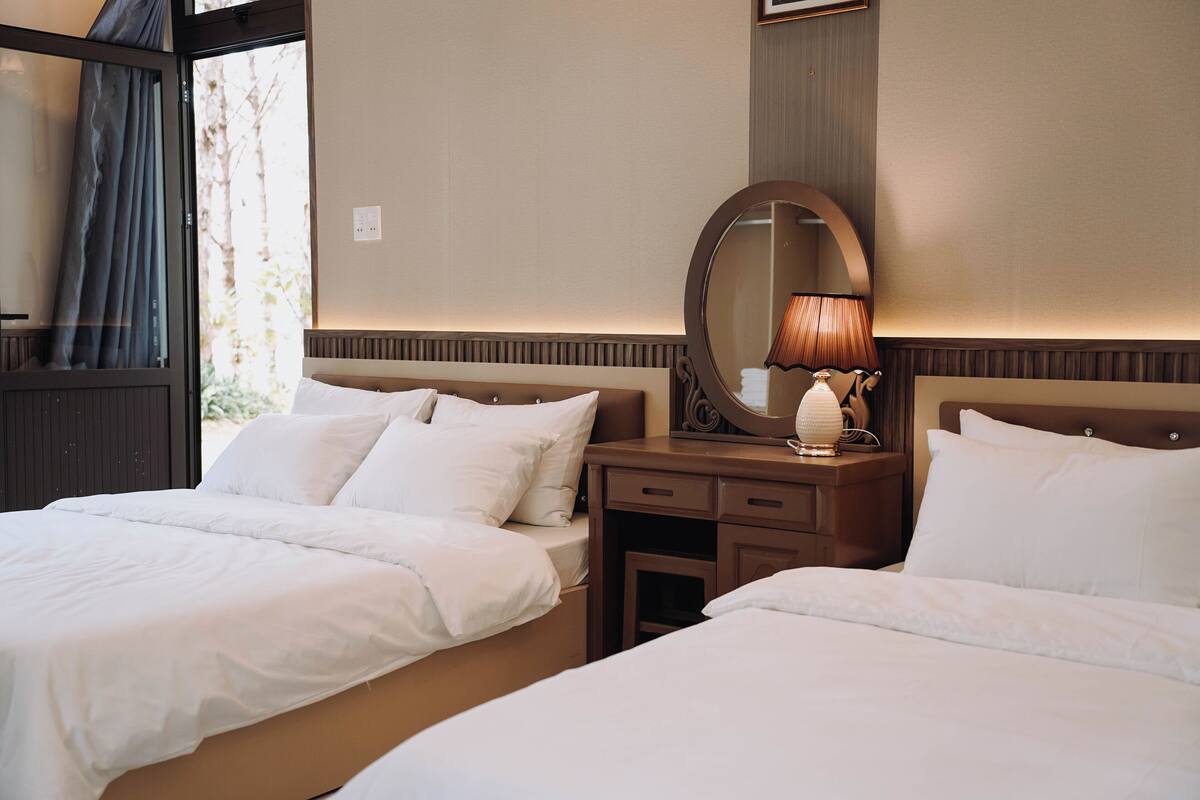Une chambre d’hôtel avec deux lits, un grand miroir, une table de chevet avec une lampe et une fenêtre avec des rideaux.