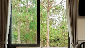 Una habitación con ventana que da a un bosque, un banco acolchado y un televisor montado en la pared.