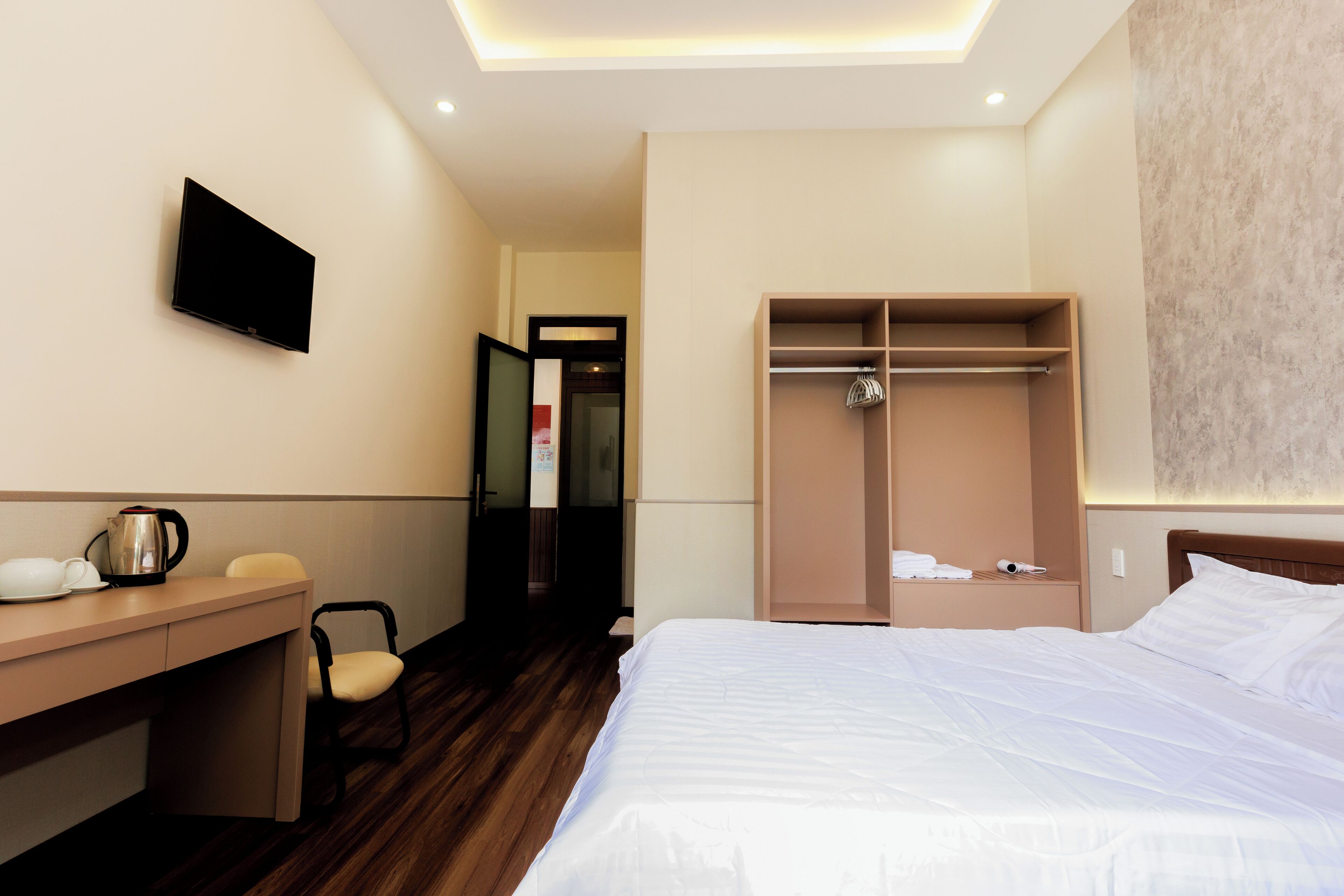 A hotel room with a bed, a desk, a chair, a wardrobe, and a television.