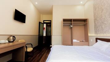 A hotel room with a bed, a desk, a chair, a wardrobe, and a television.