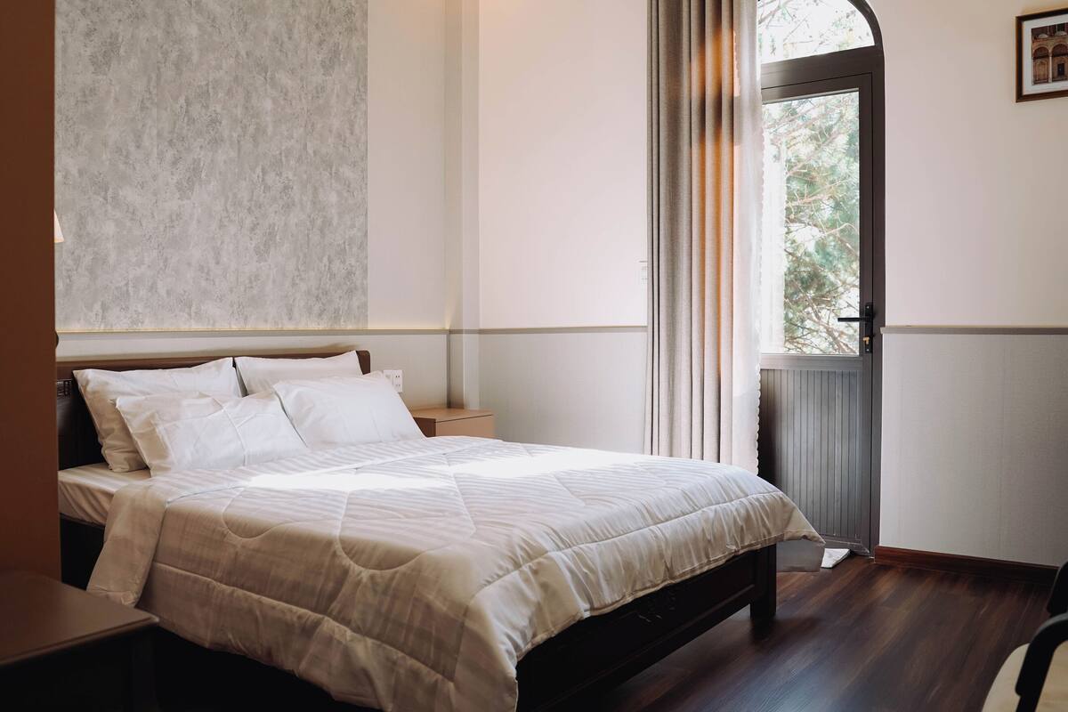 Une chambre à coucher avec un lit, des tables de chevet, une fenêtre avec des rideaux et un radiateur.