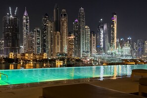 A nighttime cityscape with a pool area in the foreground. - Luxury Branded Suite with Beach Access & Sea Views (Dubai)