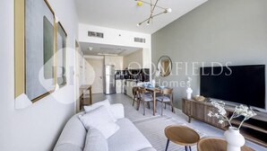 Een moderne woonkamer met een grijze bank, een eettafel met stoelen, een televisie en een decoratieve vaas.