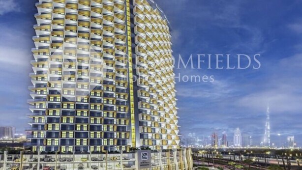 Een modern hoog gebouw met een opvallende geometrische gevel, waarschijnlijk een hotel of wooncomplex, met meerdere balkons en een uitzicht op de stadshemel op de achtergrond.