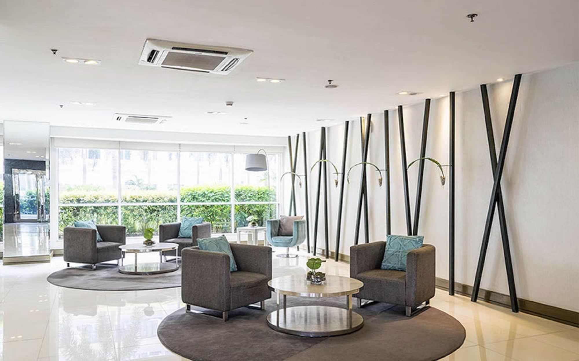 Een moderne lobby met grijze banken, een ronde salontafel en een groot raam met uitzicht op groen.