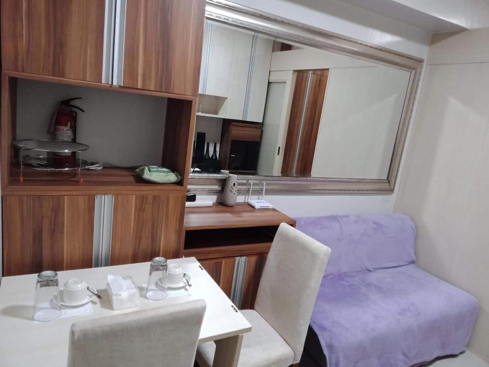 A compact room with a dining table, chairs, a purple sofa, a mirror, and wooden cabinets.