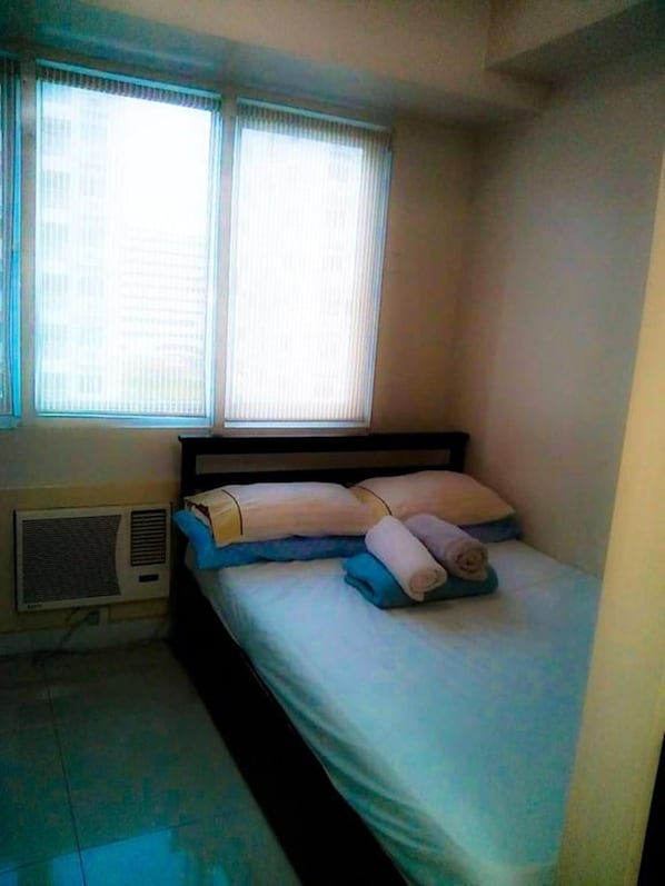 A single bed with a headboard, a window with blinds, and an air conditioning unit on the wall.
