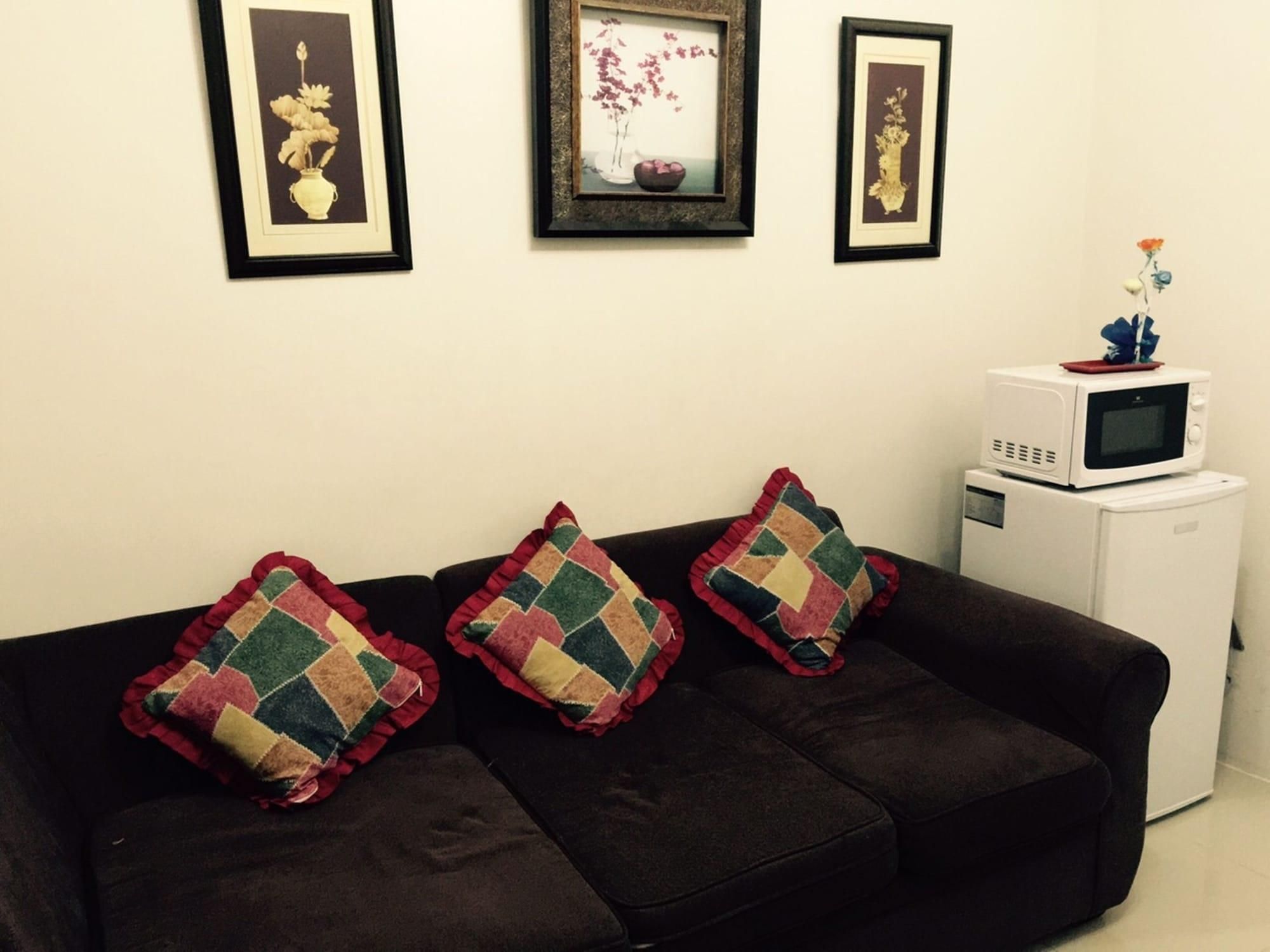 Una sala de estar con un sofá marrón oscuro, tres almohadones de colores y un microondas blanco sobre un pequeño electrodoméstico blanco.