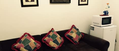 Una sala de estar con un sofá marrón oscuro, tres almohadones de colores y un microondas blanco sobre un pequeño electrodoméstico blanco.