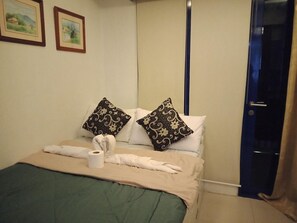 A neatly made bed with a green bedspread, two decorative pillows, a rolled towel, and a roll of toilet paper. - Jericho's Place at Sea Residences (Pasay)