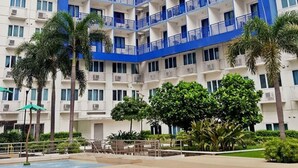 A high-rise hotel with multiple balconies, a swimming pool, and palm trees. - Jericho's Place at Sea Residences (Pasay)