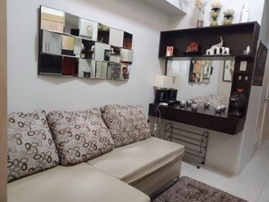 A living room with a sofa, a coffee table, a side table, a lamp, and a wall-mounted mirror. - Jericho's Place at Sea Residences (Pasay)