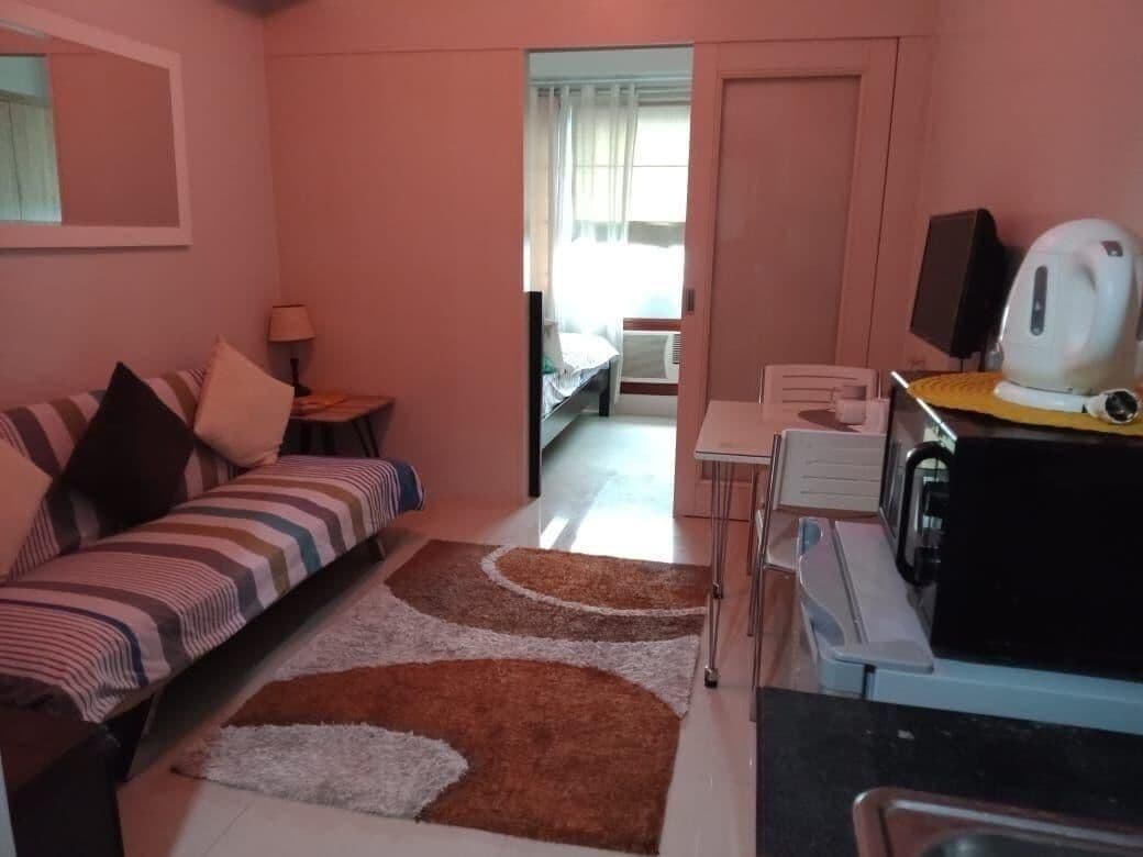 A small room with a bed, a desk, a kettle, and a radiator.