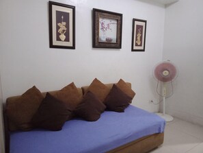 A bedroom with a bed, pillows, a wall-mounted fan, and three framed pictures. - Jericho's Place at Sea Residences (Pasay)