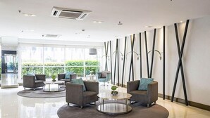 A modern lobby with grey sofas, a round coffee table, and a large window offering a view of greenery. - Jericho's Place at Sea Residences (Pasay)