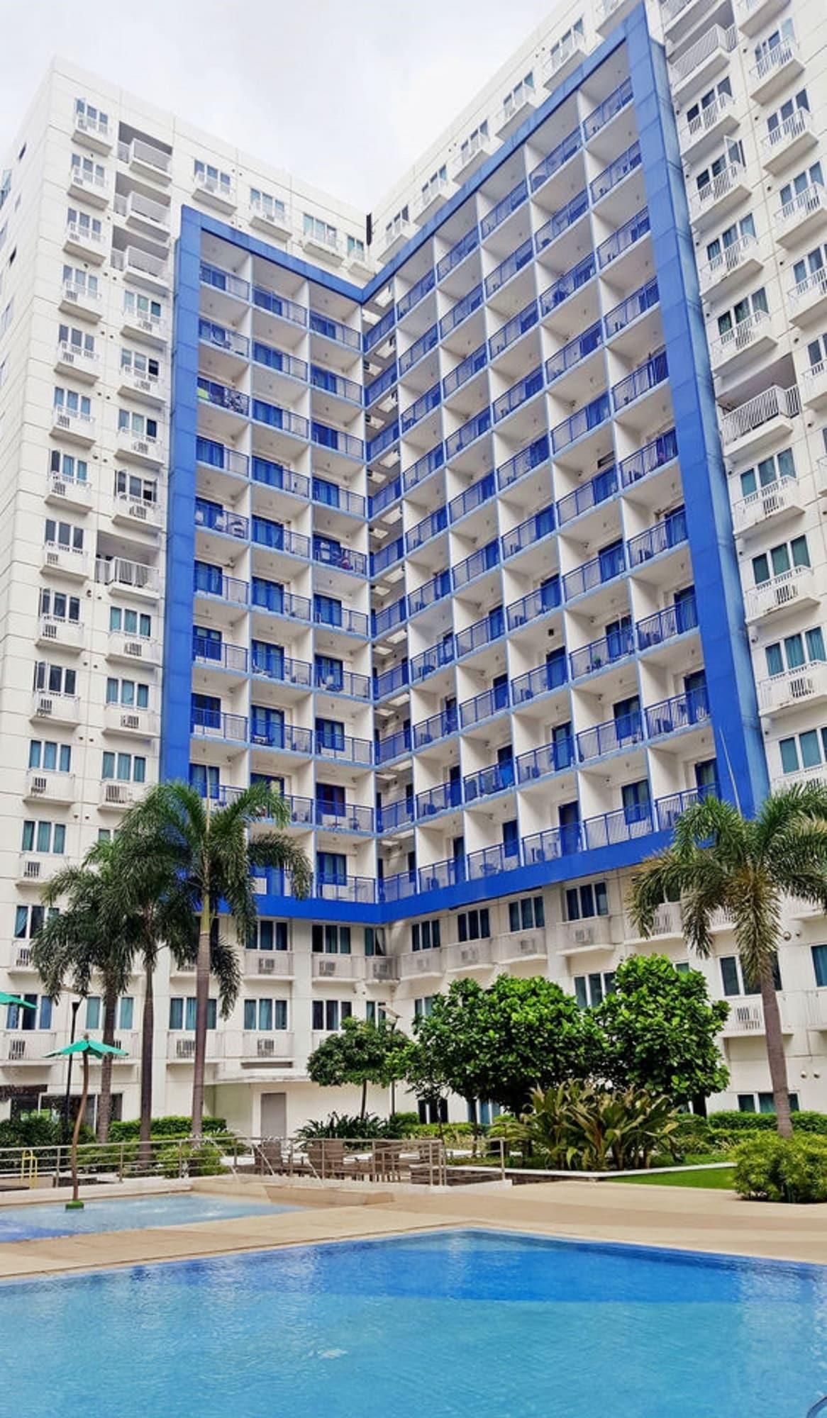 A high-rise hotel with multiple balconies, a swimming pool, and palm trees.