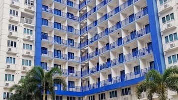 A high-rise hotel with multiple balconies, a swimming pool, and palm trees.