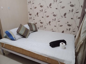 A single bed with a white mattress, two patterned pillows, a rolled-up black towel, and a roll of white toilet paper. - Jericho's Place at Sea Residences (Pasay)