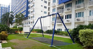 A residential building with multiple balconies, a swing set, and well-maintained greenery. - Jericho's Place at Sea Residences (Pasay)