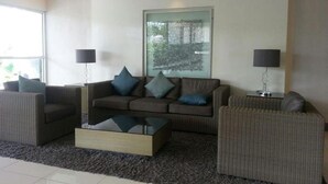 A modern living room with a sofa set, two side tables with lamps, a coffee table, and a large window with a view of trees. - Jericho's Place at Sea Residences (Pasay)