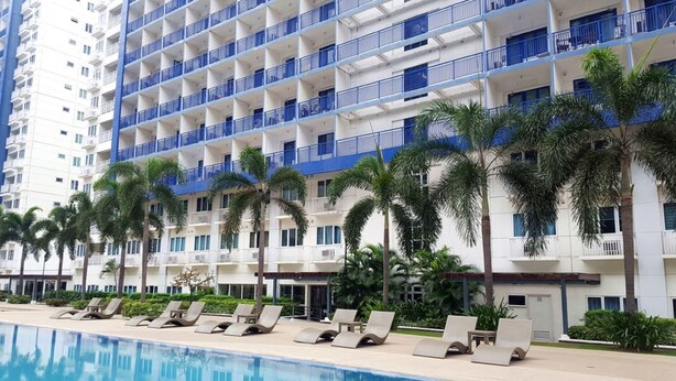A high-rise hotel with multiple balconies, a swimming pool, and palm trees. - Jericho's Place at Sea Residences (Pasay)