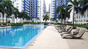 A swimming pool with lounge chairs, surrounded by palm trees and modern buildings.