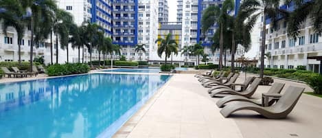 Una piscina con sillas de descanso, rodeada de palmeras y edificios modernos.