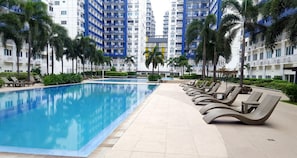 A swimming pool with lounge chairs, surrounded by palm trees and modern buildings. - Jericho's Place at Sea Residences (Pasay)