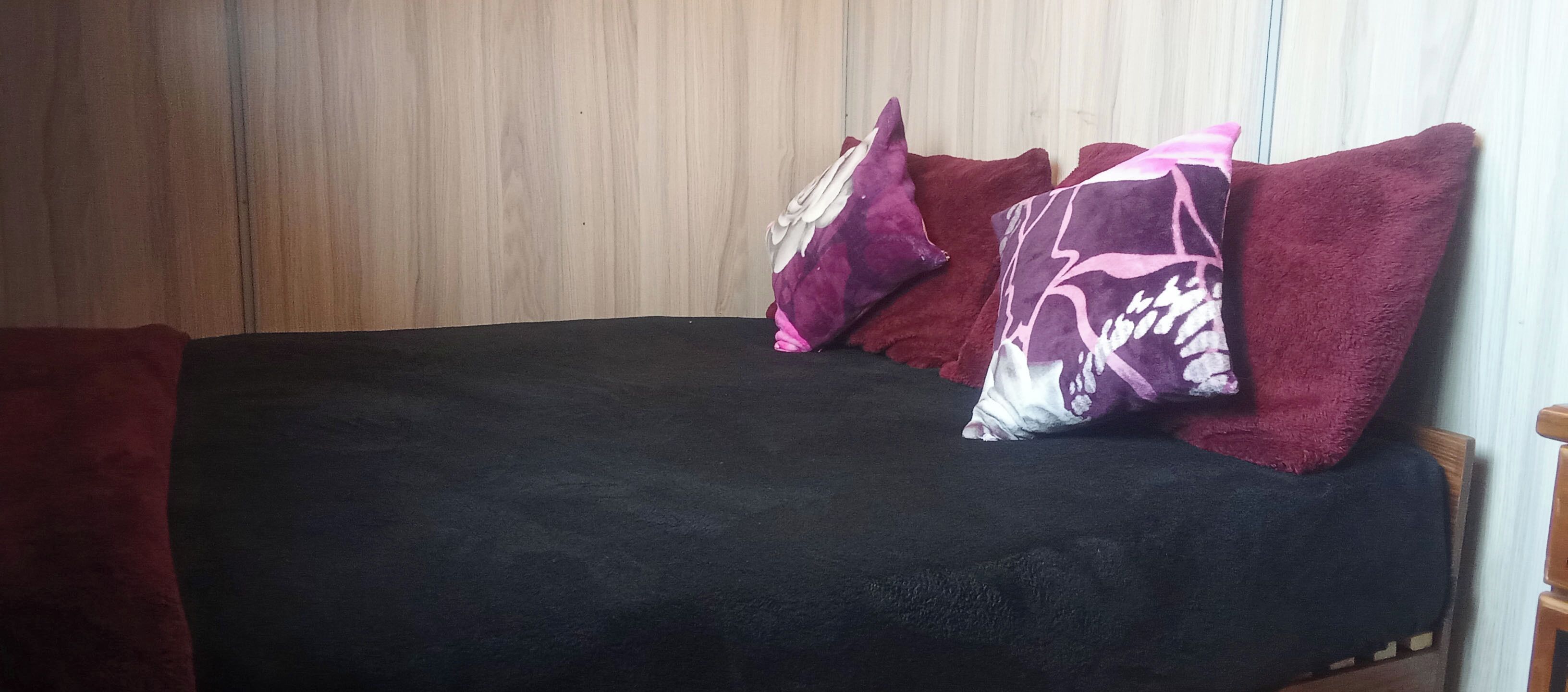 A bed with a black mattress and multiple pillows, including a purple one with a white pattern.